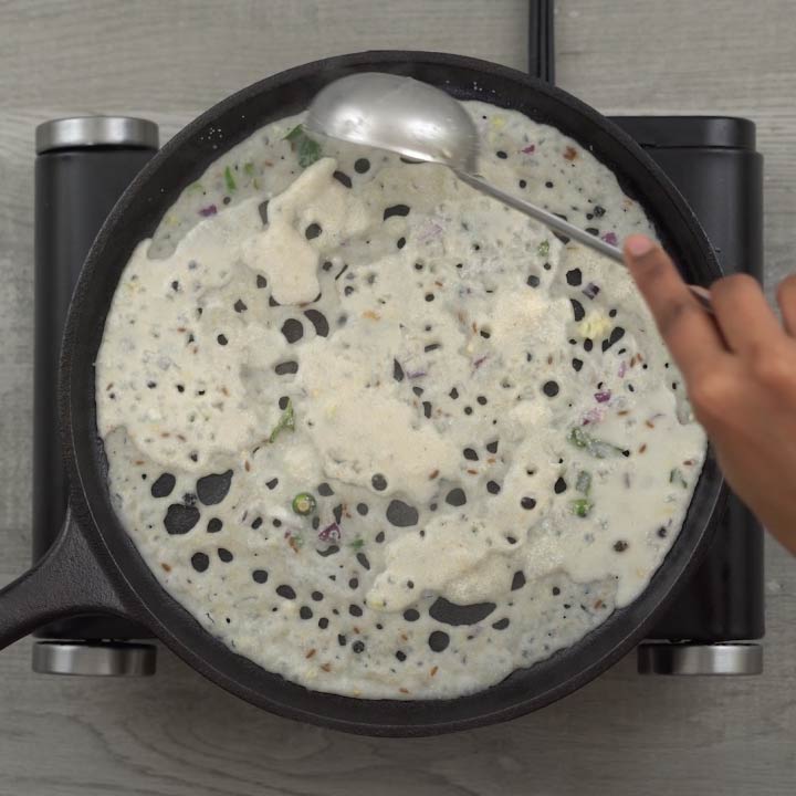 Pouring rava dosa batter in hot cast iron