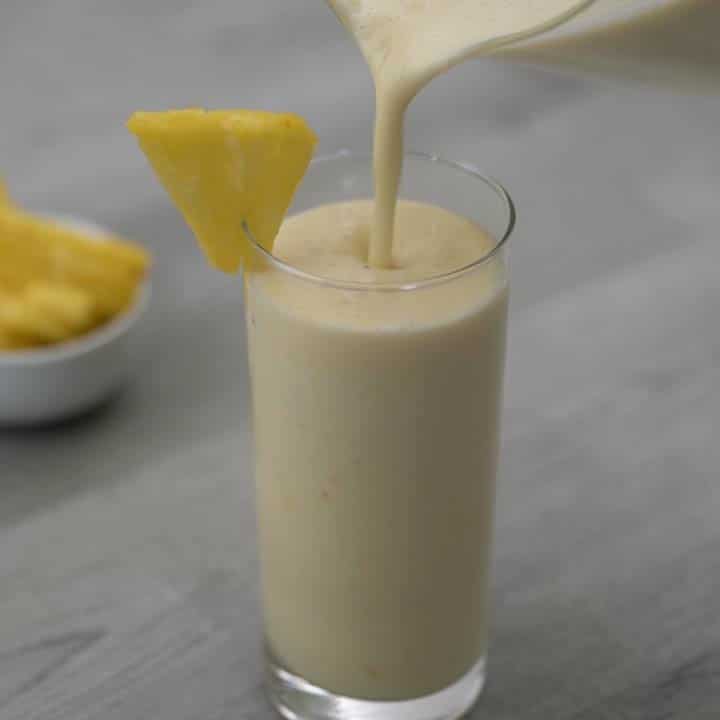 Pouring the pineapple smoothie into a serving glass.