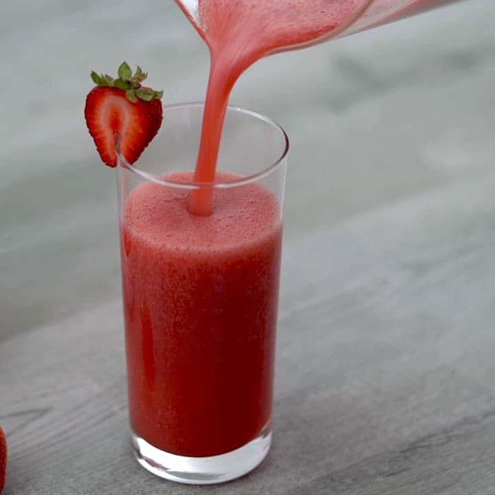 Pouring healthy strawberry juice into a serving glass.