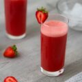 Strawberry Juice in a serving glass with strawberries around.