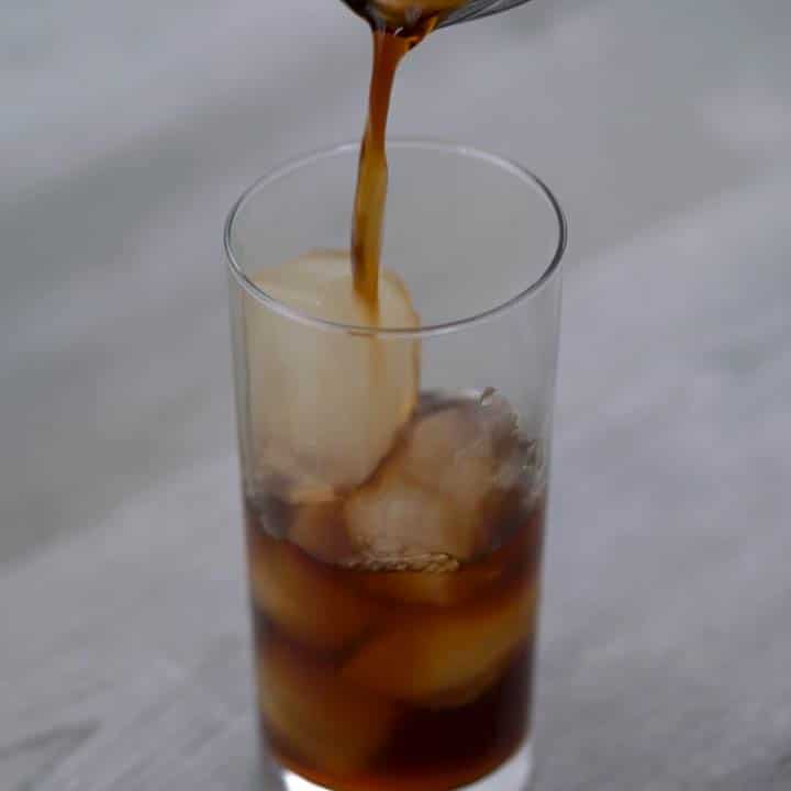 Pouring the chilled black coffee over ice cubes.