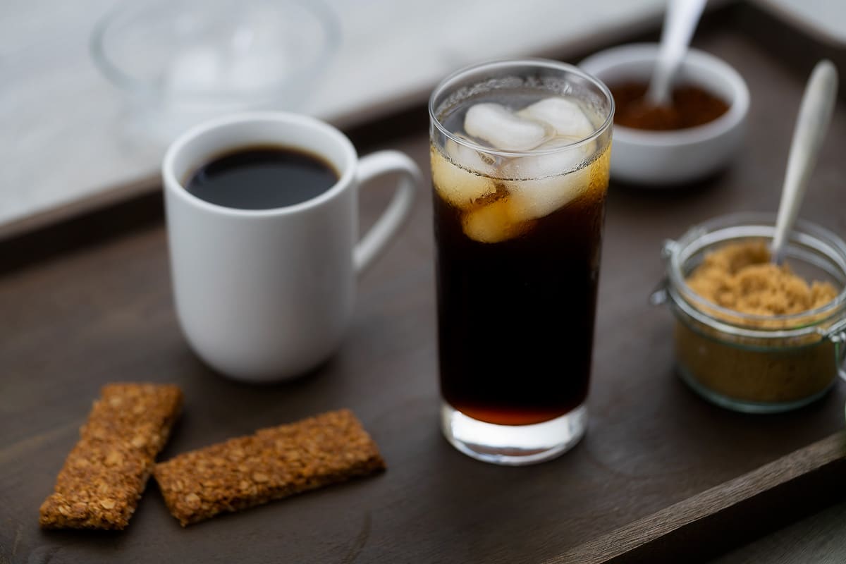 Hot and Iced Black Coffee served in a glass and coffee cup with snacks alongside.