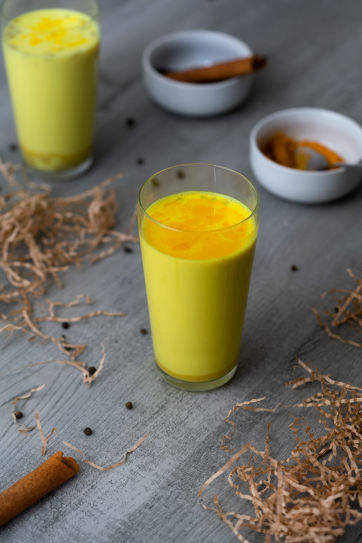 Golden Milk also called turmeric milk served in a serving glass with peppercorns around.