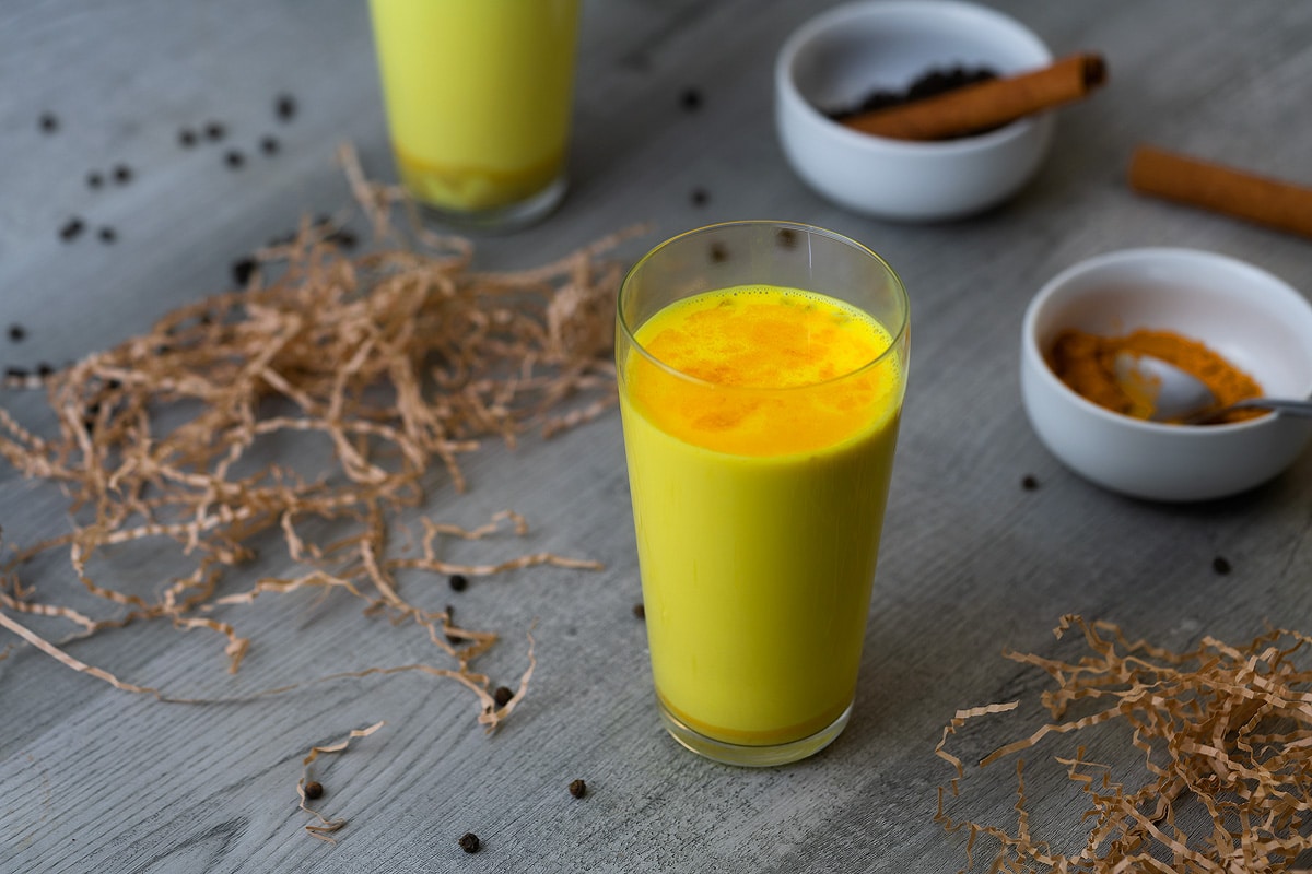 Golden Milk also called turmeric milk served in a serving glass with peppercorns around.