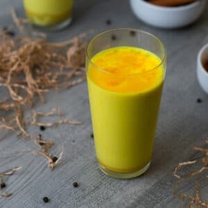 Golden Milk also called turmeric milk served in a serving glass with peppercorns around.