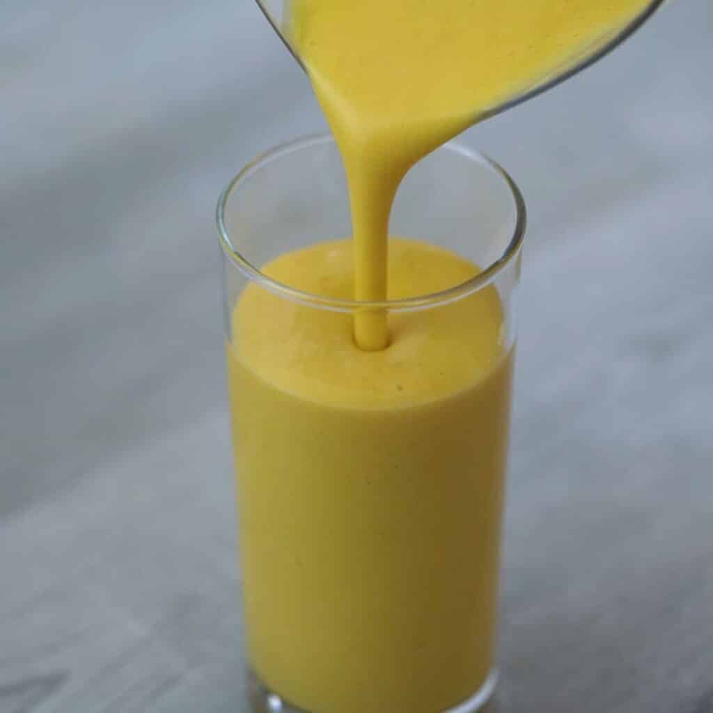 Pouring Mango Lassi into a serving glass.