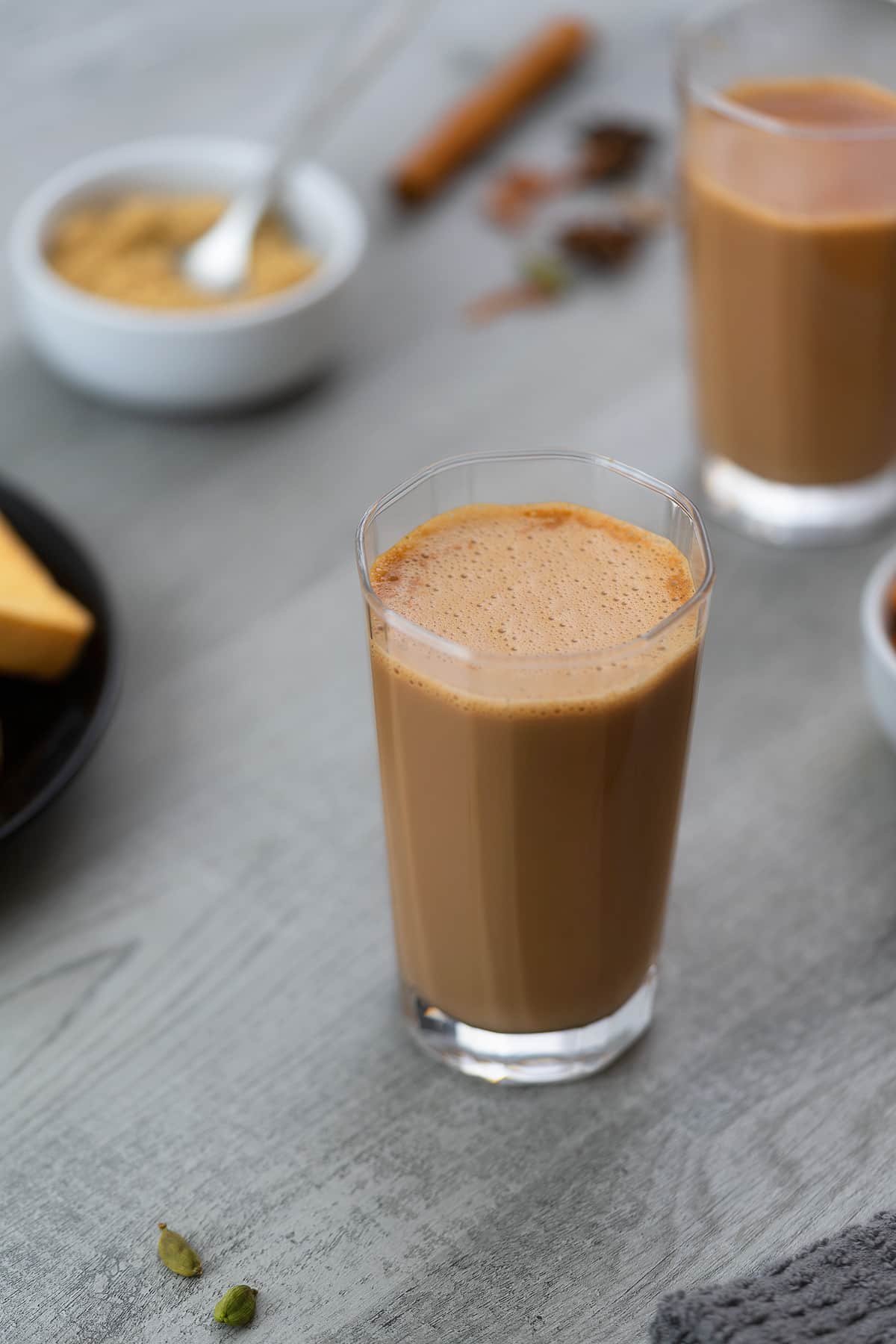 Masala Chai (tea) served in a glass with sugar and spices placed around.