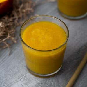 Mango Juice served in a glass with straw and mango nearby.