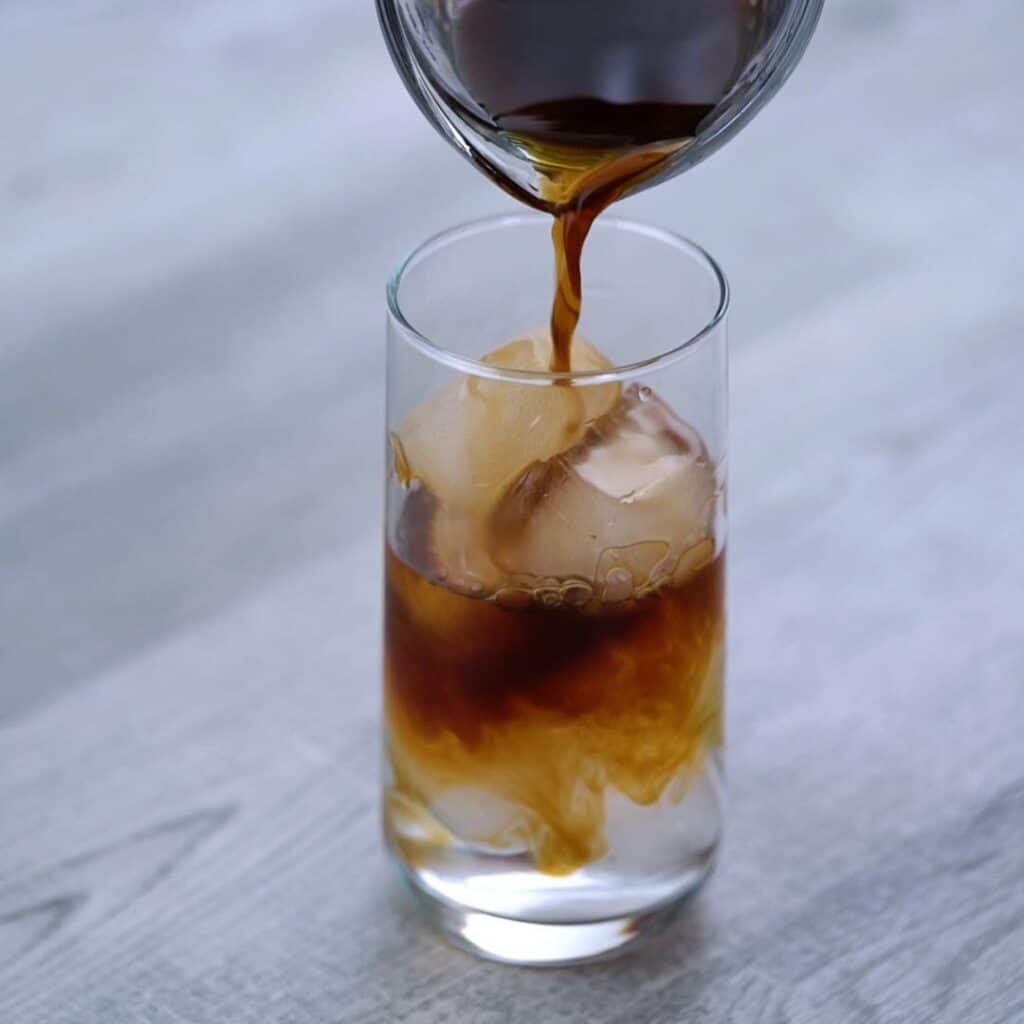 Pouring cold brew coffee over ice in to glass.