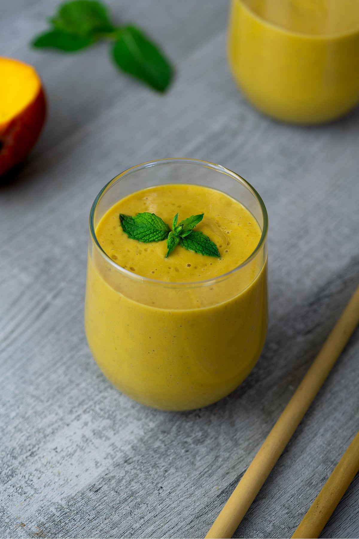 Mango Smoothie garnished with mint leaves in a serving glass. 
