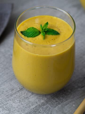 Mango Smoothie garnished with mint leaves in a serving glass.