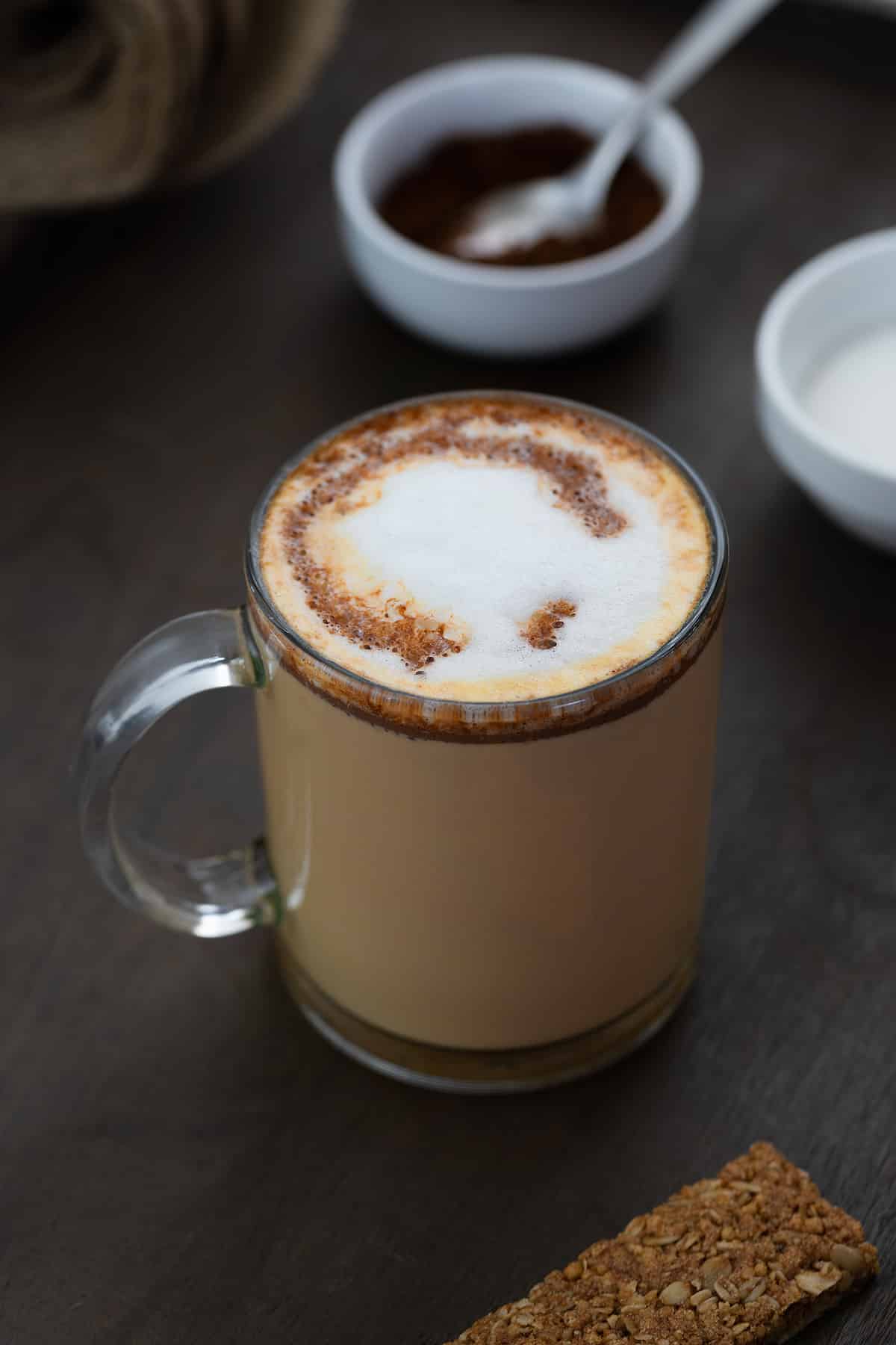 Mocha Coffee served in a glass mug with coffee powder placed in a bowl nearby.