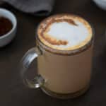 Mocha Coffee served in a glass mug with coffee powder placed in a bowl nearby.