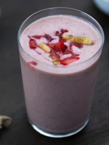 Strawberry Banana Smoothie is served in a glass with strawberries and banana nearby.