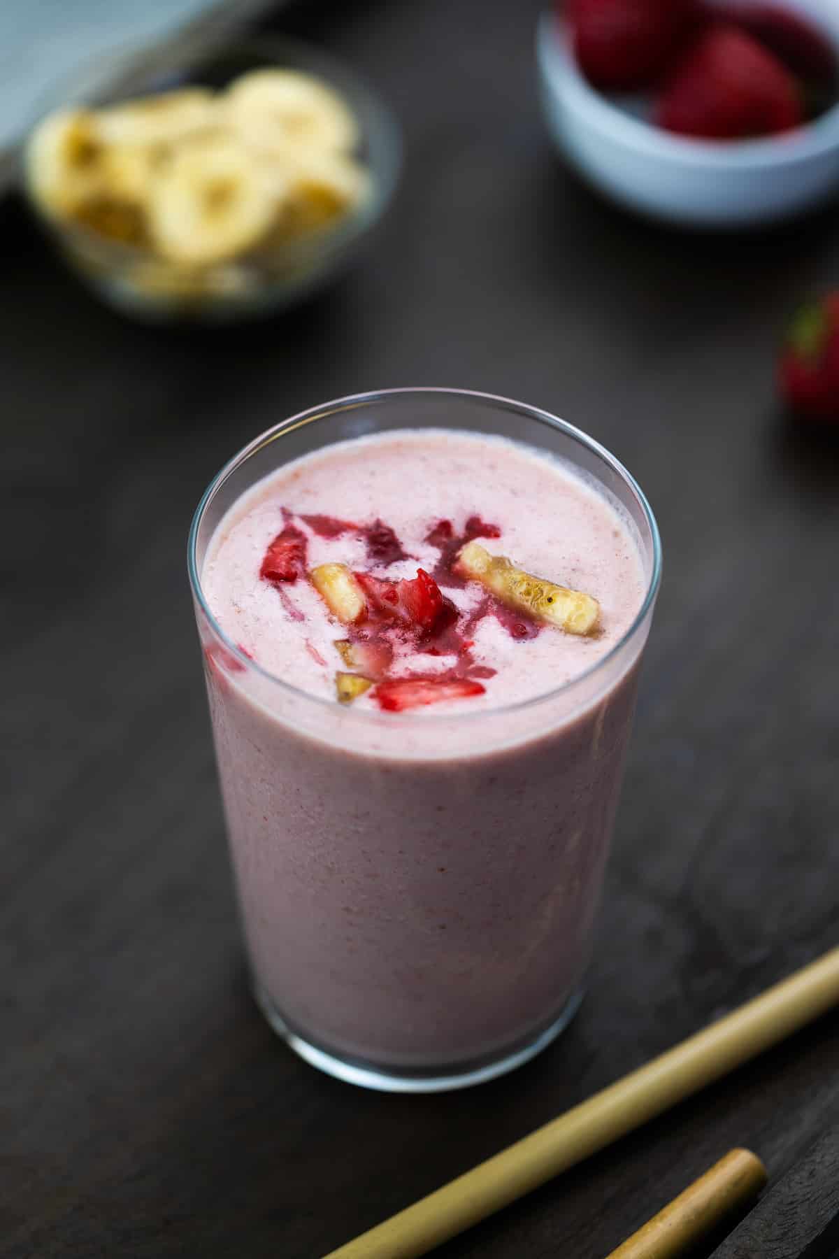 Strawberry Banana Smoothie is served in a glass with strawberries and banana nearby.