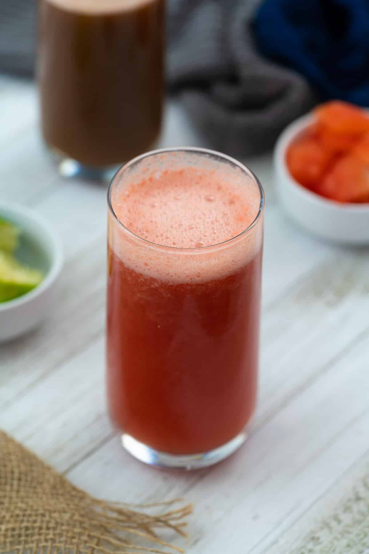Fresh watermelon juice served in glass with watermelon and lemon nearby.