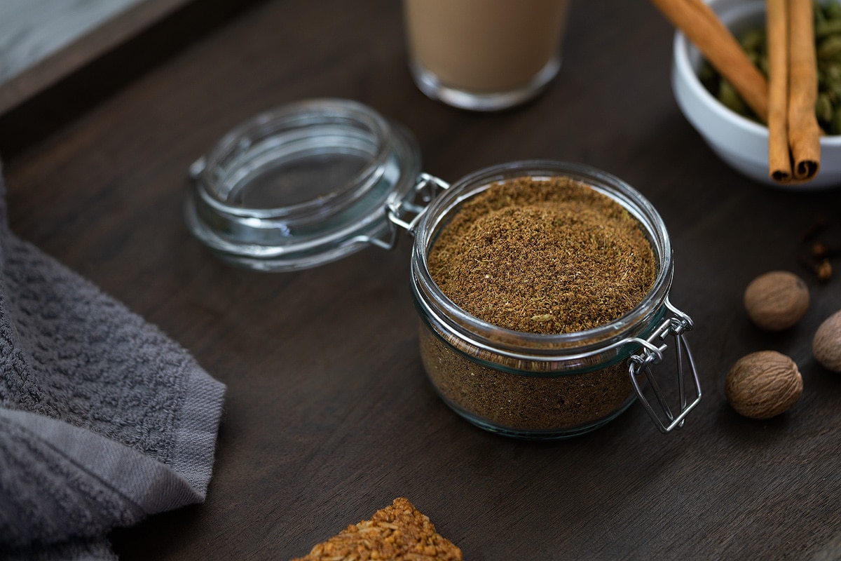 Chai Masala Powder in a jar with few spices placed nearby.