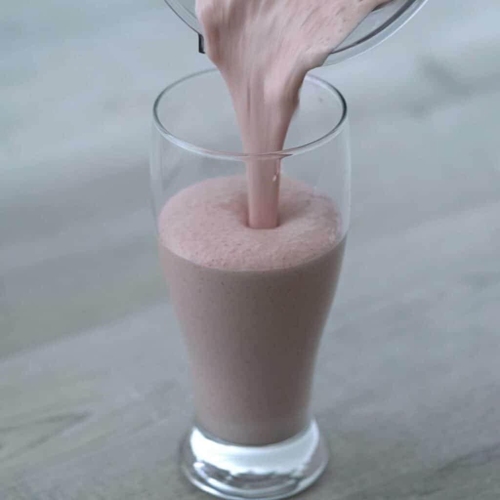 Pouring strawberry milkshake into glass.