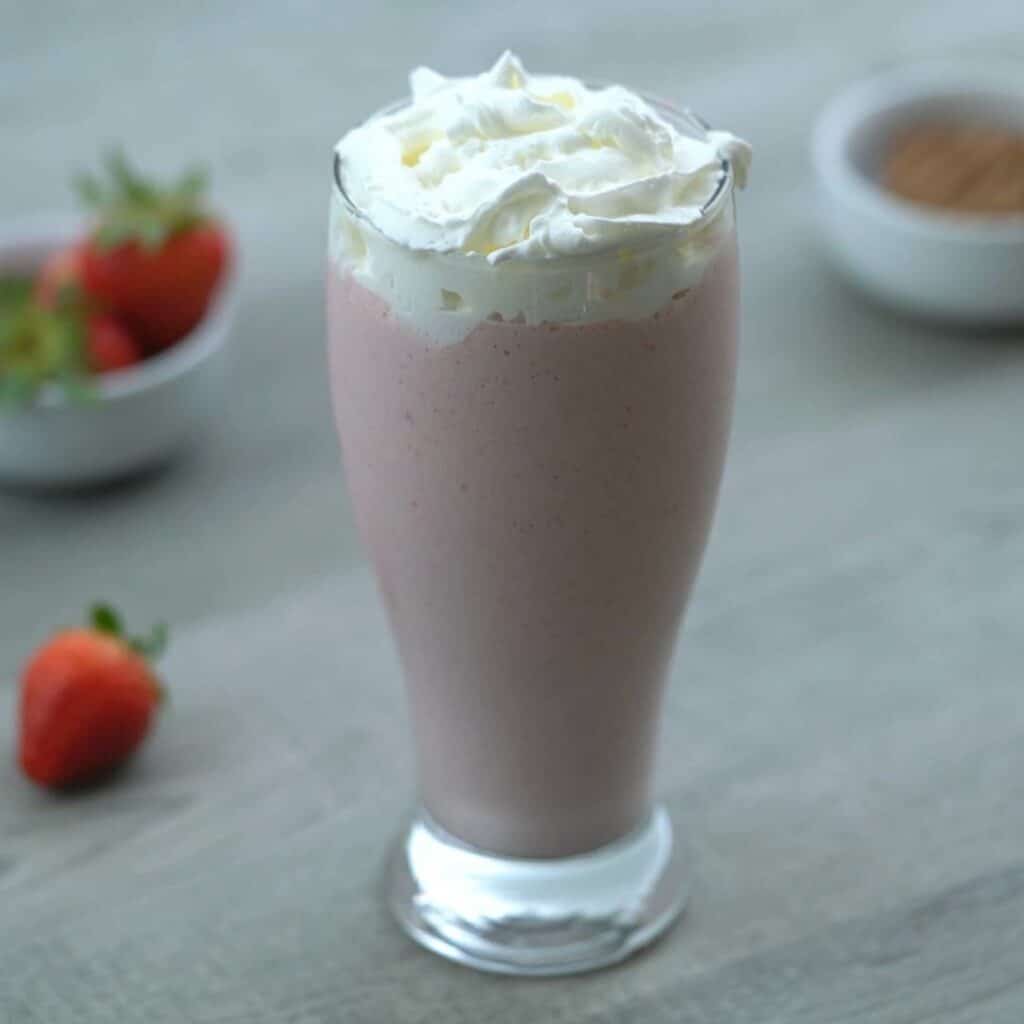 strawberry milkshake is served in a glass with whipping cream.