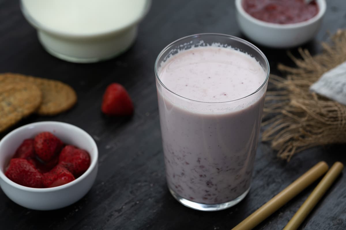 Strawberry Milk in a glass with strawberries and snacks around.