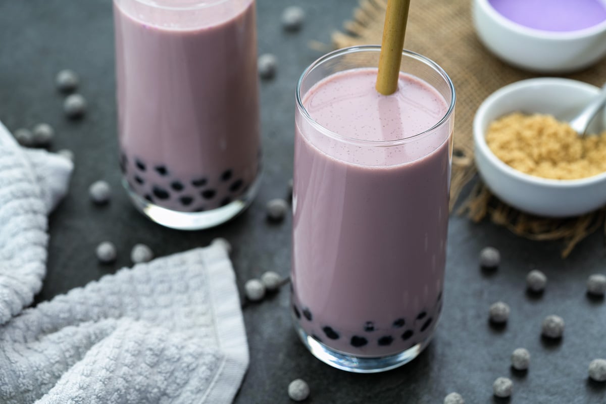 Taro Milk Tea in a tall glass with boba pearls scattered around.