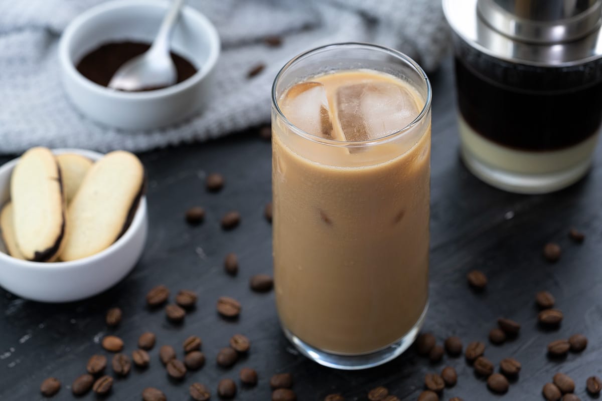 Vietnamese iced Coffee served in a tall glass with coffee beans scattered around and filter placed behind.