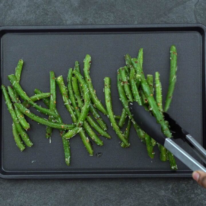 placing the seasoned green beans in a baking tray
