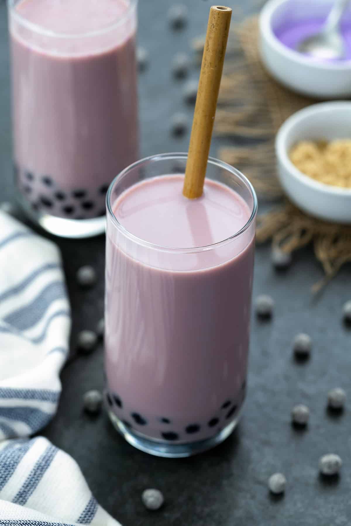 Taro Milk Tea in a tall glass with boba pearls scattered around.