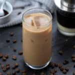 Vietnamese iced Coffee served in a tall glass with coffee beans scattered around and filter placed behind.