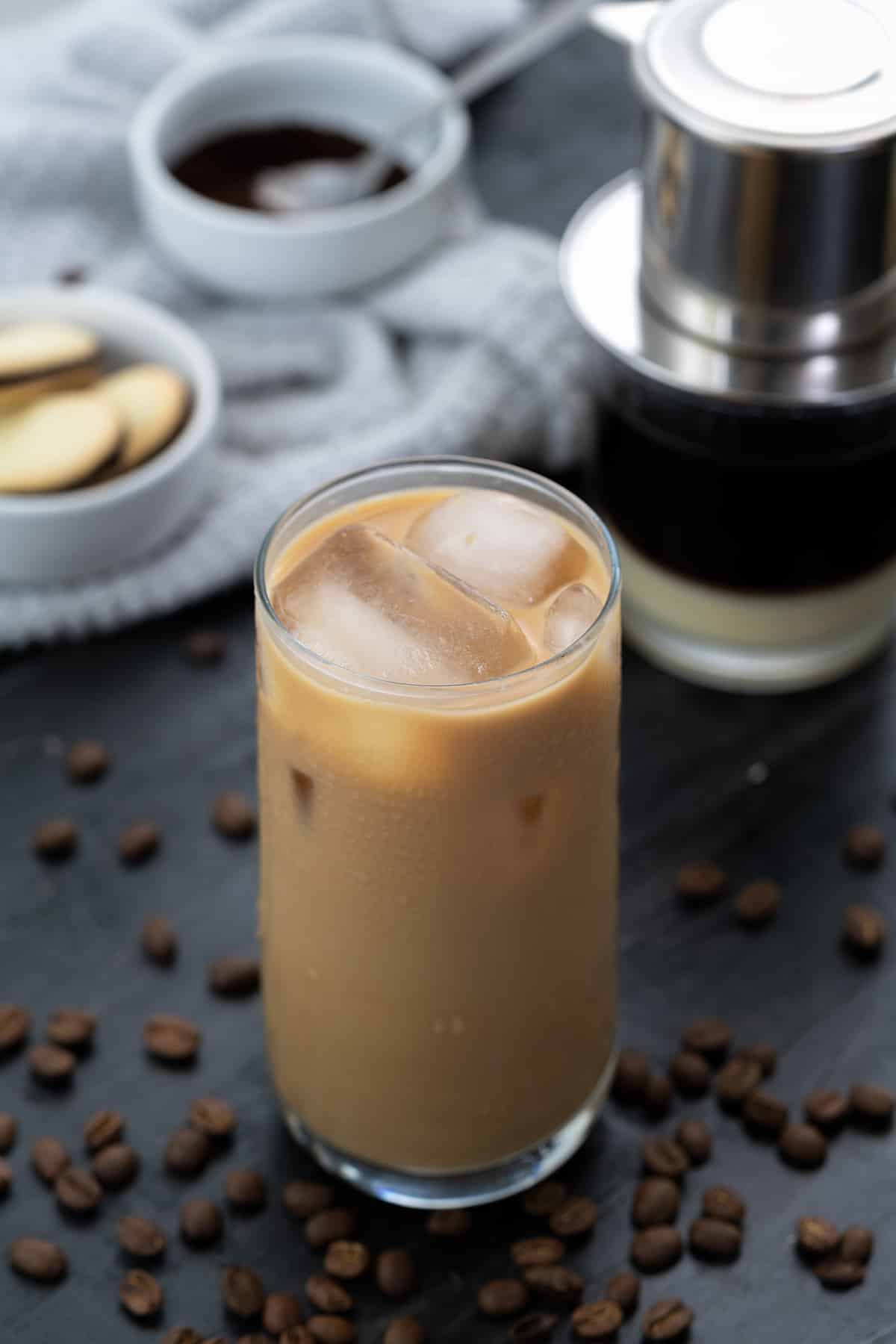 Vietnamese iced Coffee served in a tall glass with coffee beans scattered around and filter placed behind.