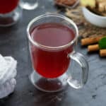 Ginger Tea served in a mug with cinnamon and mint leaves nearby.