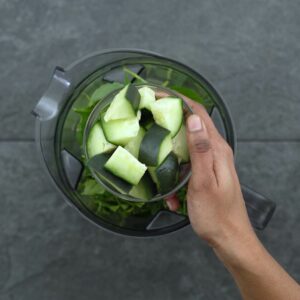 Adding cucumber and green leaves to blender jar.