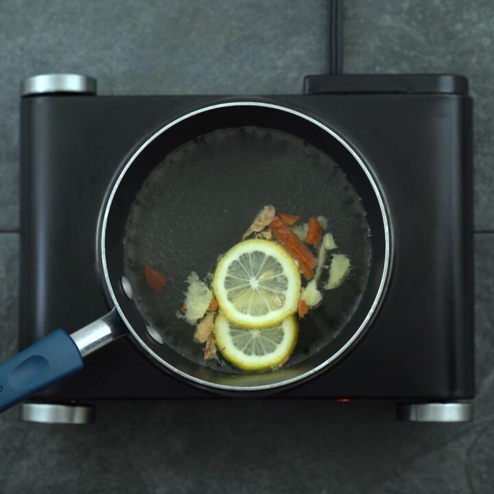 Lemon, cinnamon, ginger water boiling in saucepan.
