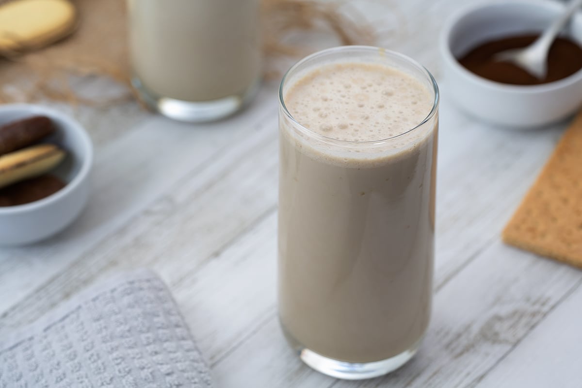 Iced Coffee Protein Shake in a glass with coffee powder and snacks placed nearby.