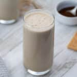 Iced Coffee Protein Shake in a glass with coffee powder and snacks placed nearby.