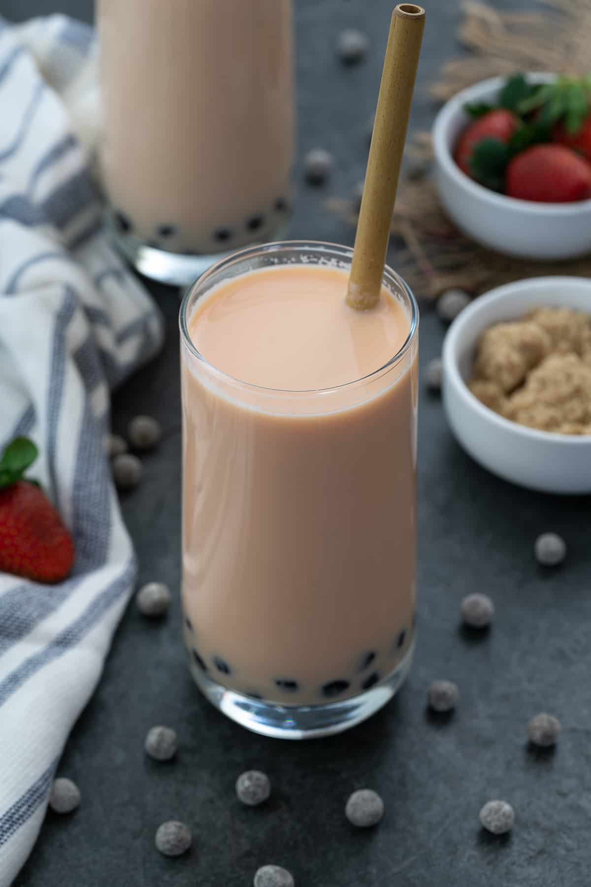 Strawberry Milk Bubble Tea served in a glass with boba pearls scattered nearby.