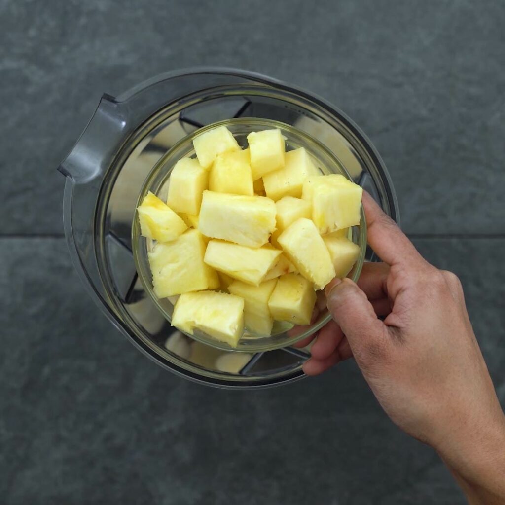Adding pineapple into the blender jar.