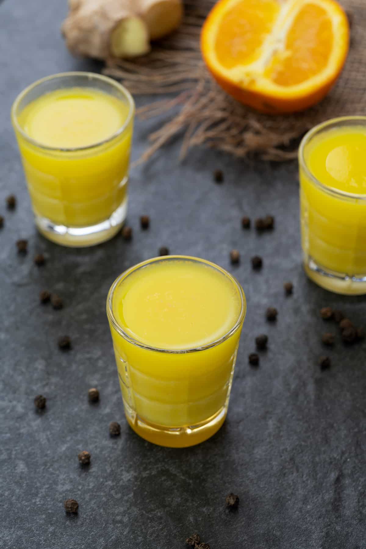 Ginger Shots served in a shots glass with peppercorns scattered around.
