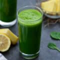 Green Juice served in a glass with lemon, greens and pineapple placed nearby.