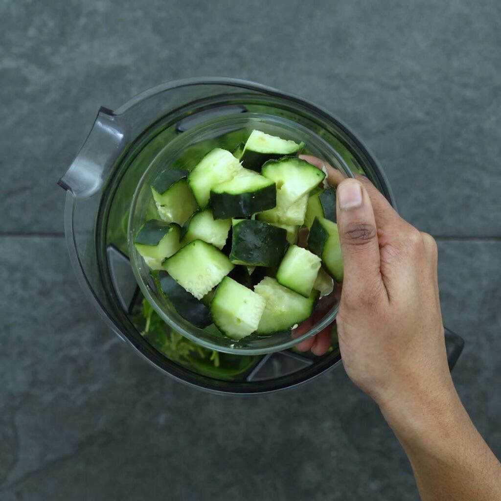 Adding cucumber into the blender greens and fruits.