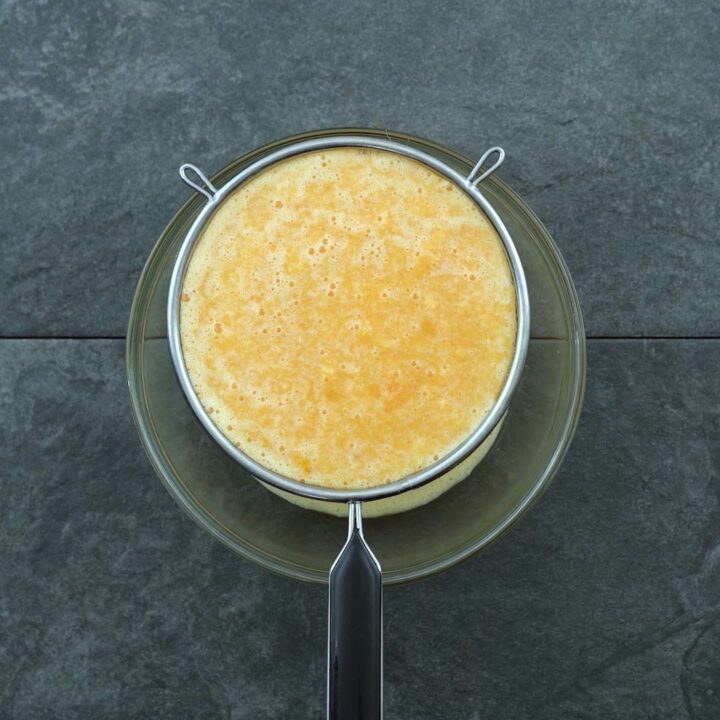 Filtering orange juice with strainer.