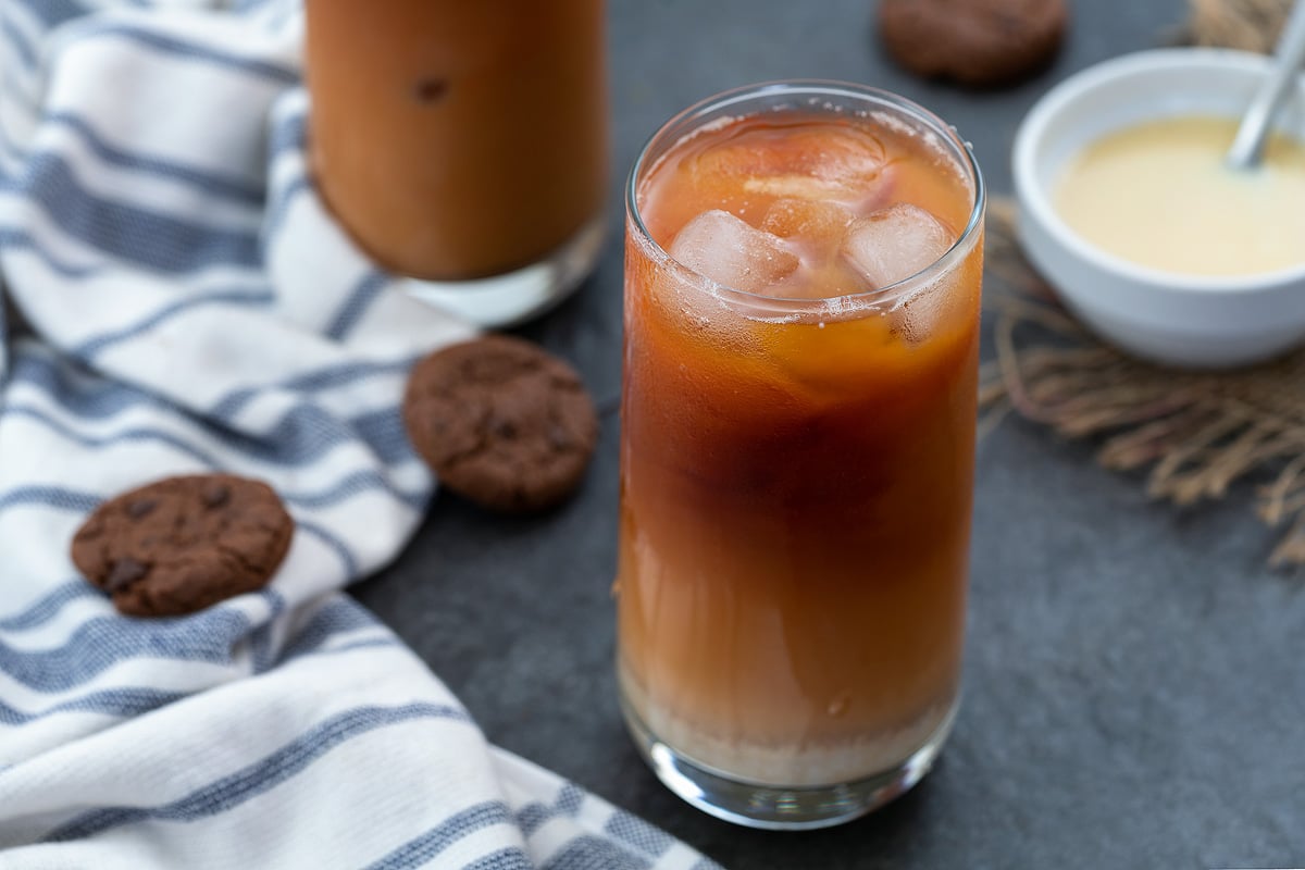 Thai Iced Tea served in a tall glass with condensed milk and cookies placed near by.