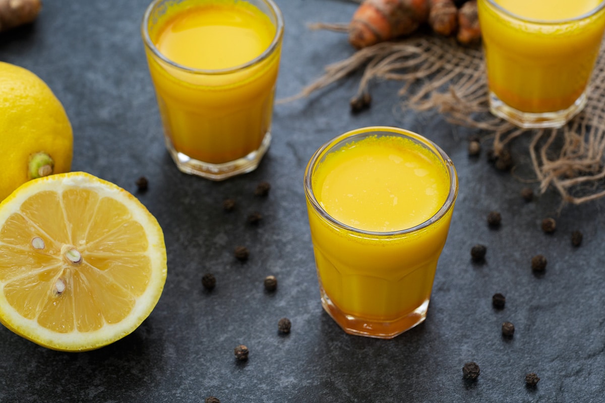 Turmeric Shots  in a shots glass with peppercorns scattered around.