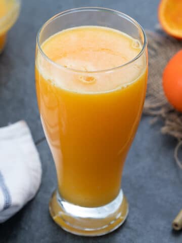 Orange Juice served in a glass with orange and cookies placed nearby.