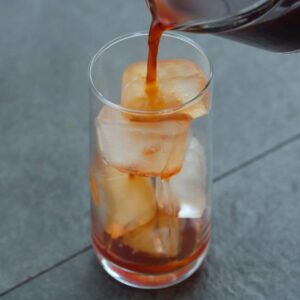 Pouring Thai tea into a ice filled serving glass.