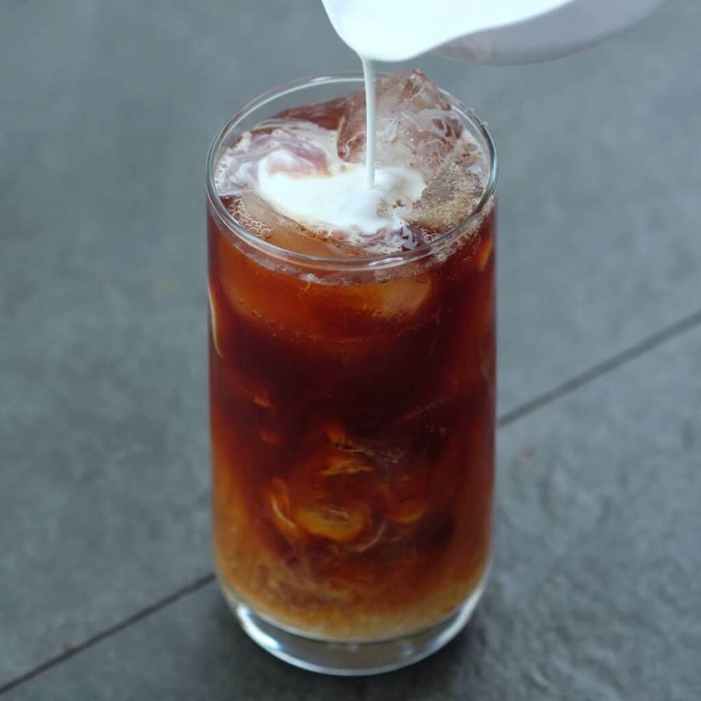 Pouring half and half milk to Thai iced tea.