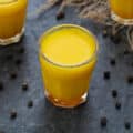 Turmeric Shots in a shots glass with peppercorns scattered around.