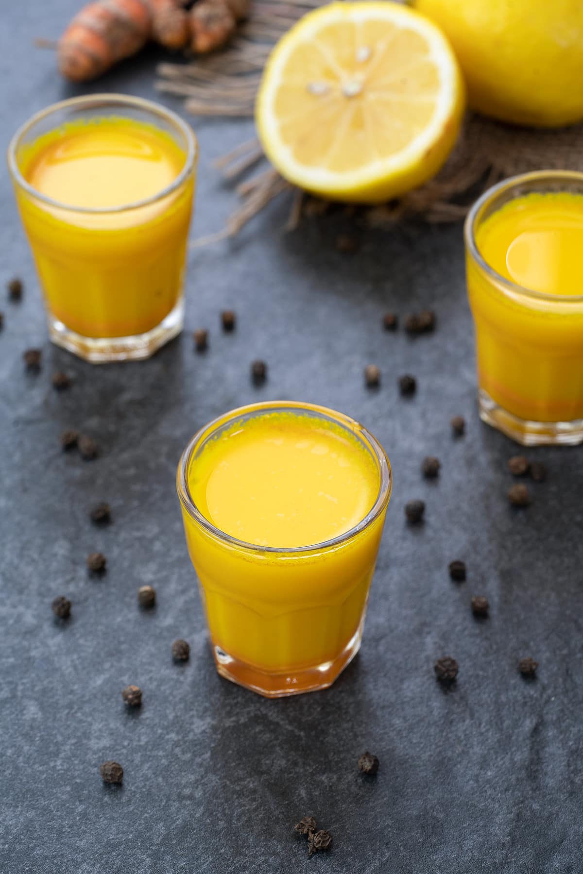 Turmeric Shots  in a shots glass with peppercorns scattered around.