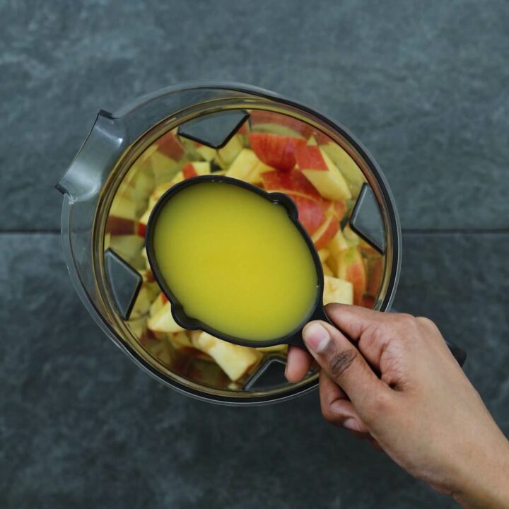 Adding orange juice to apples in blender.