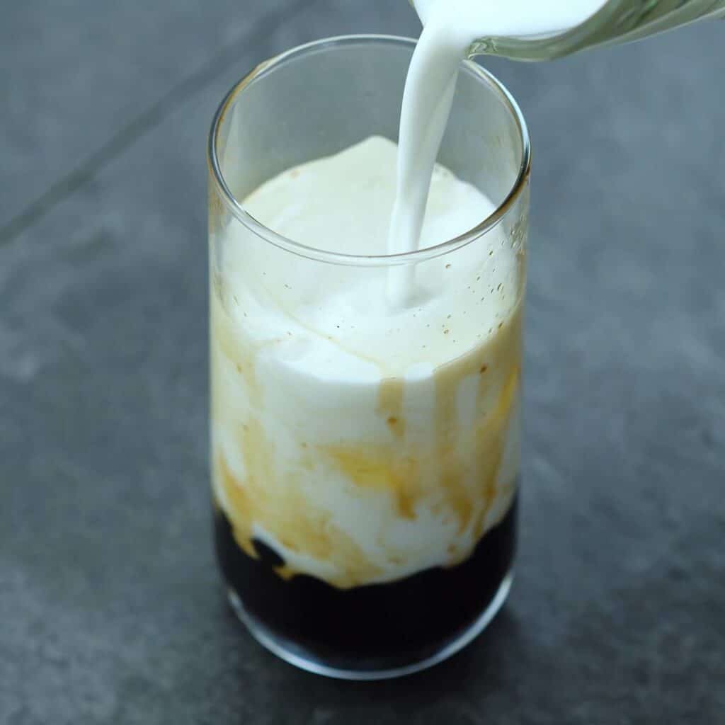 Pouring milk to brown sugar boba in a glass.